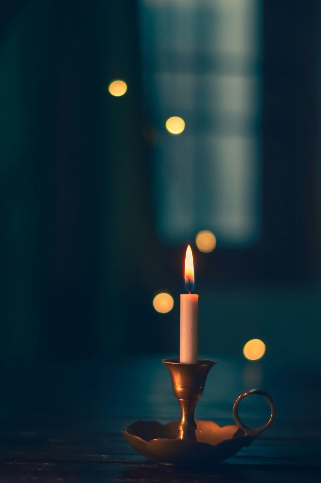 A warm candle flame on a brass holder in low light